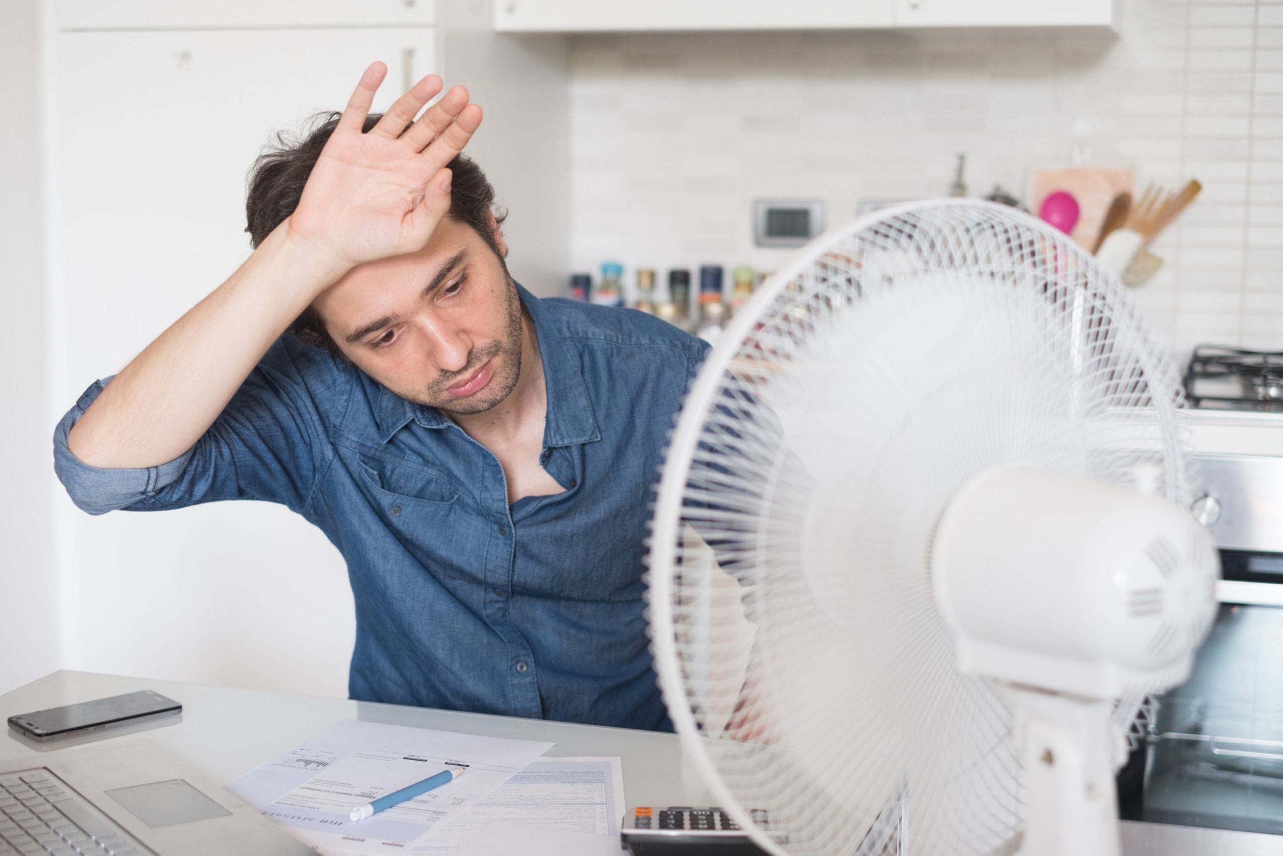 Sweaty man trying to refresh from heat with a fan